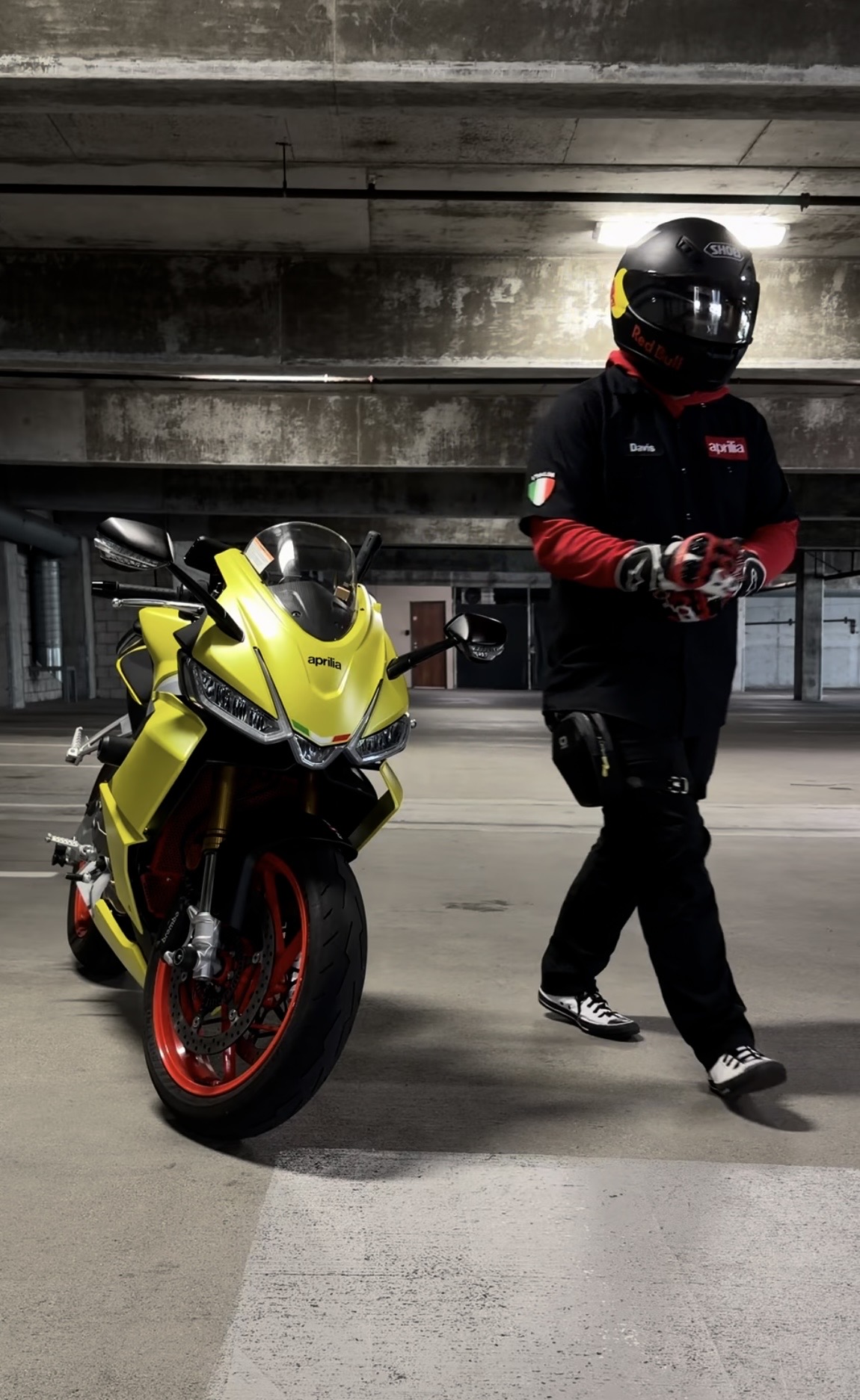 Yellow Aprilia RS660 with red wheels and rider in black gear in underground parking garage